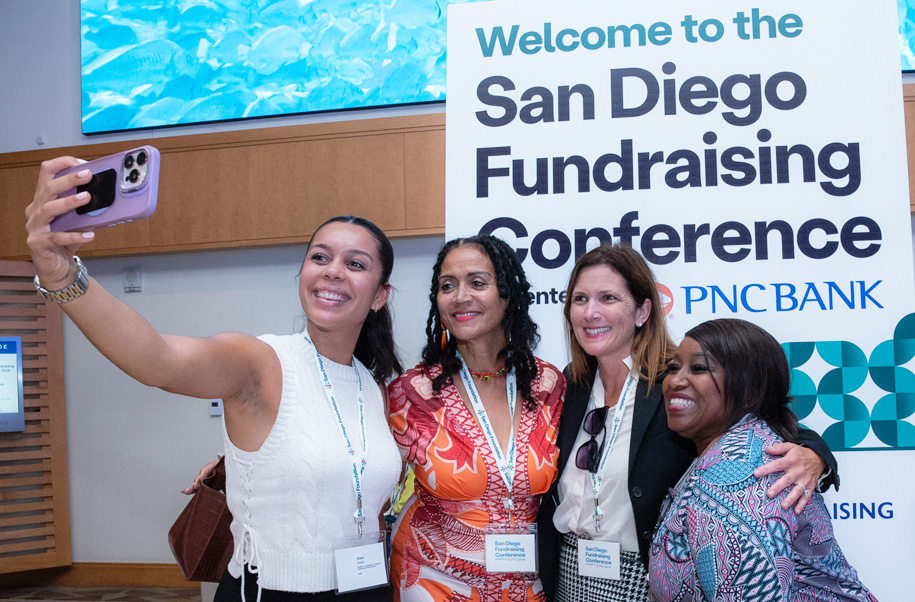 A group of women take a selfie in front ofa San Diego Fundraising Conference sign