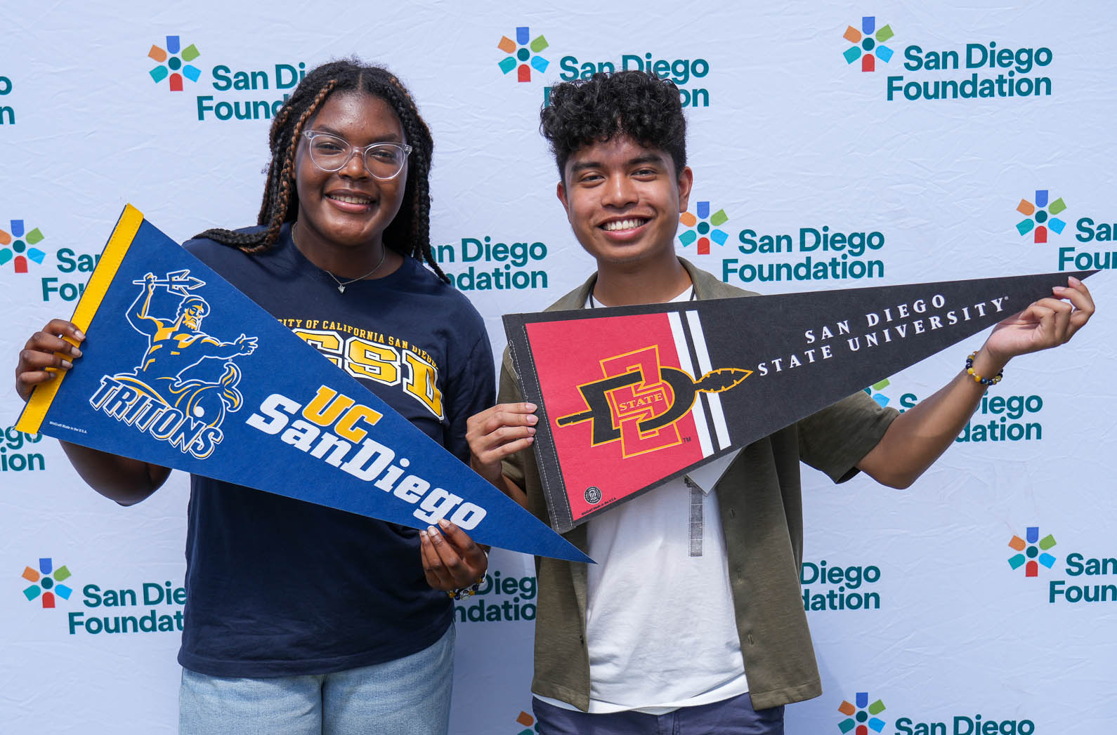 Two students holding San Diego pennants in front of a San Diego Foundation banner